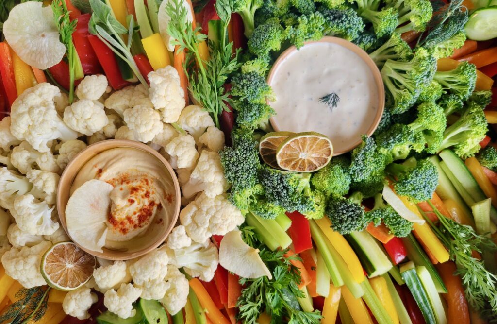 An assortment of vegetables set around 2 dip bowls with dehydrated limes for garnish