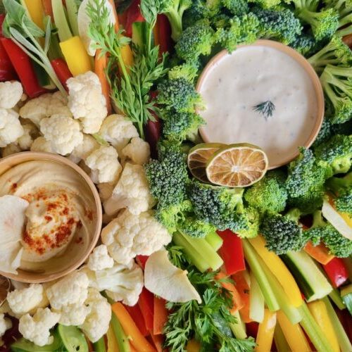 An assortment of vegetables set around 2 dip bowls with dehydrated limes for garnish